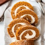 A sliced pumpkin roll dessert on a white serving platter.