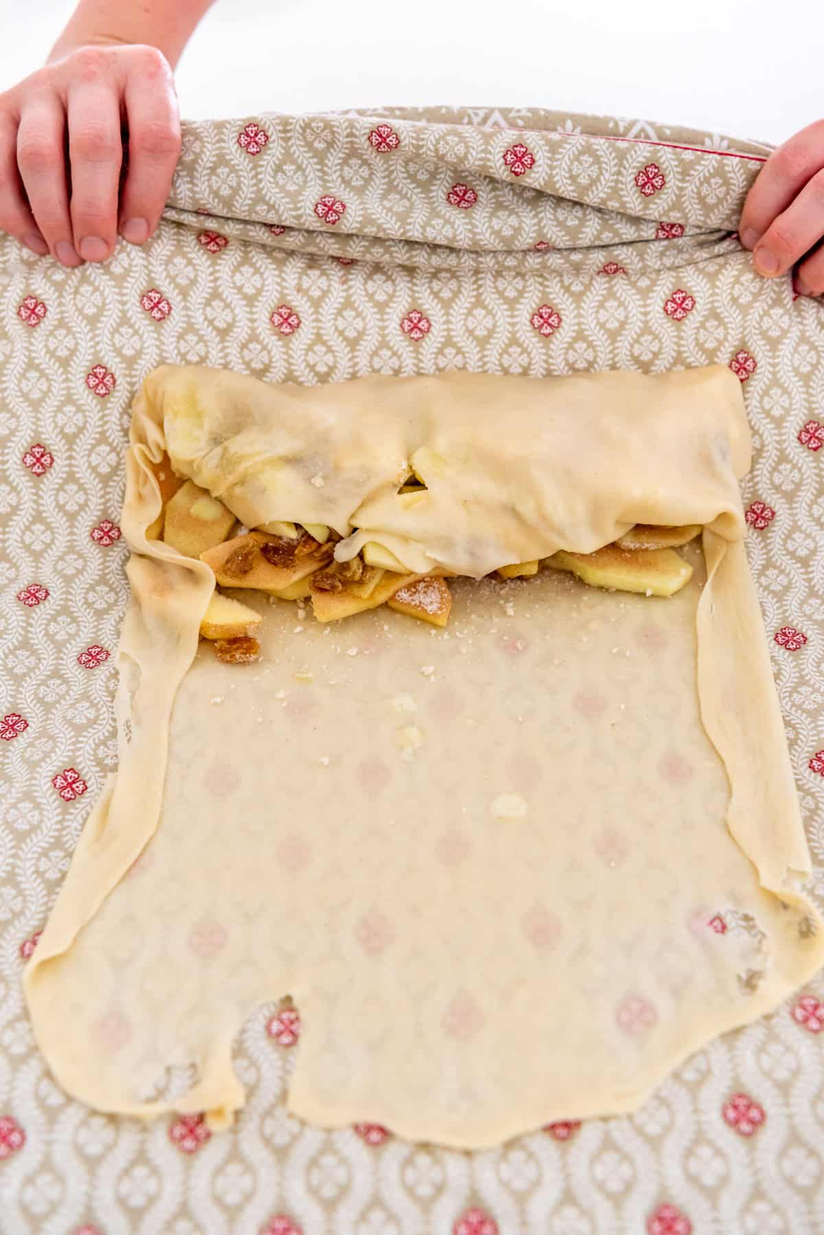 hands using a tablecloth to roll up an apple strudel.