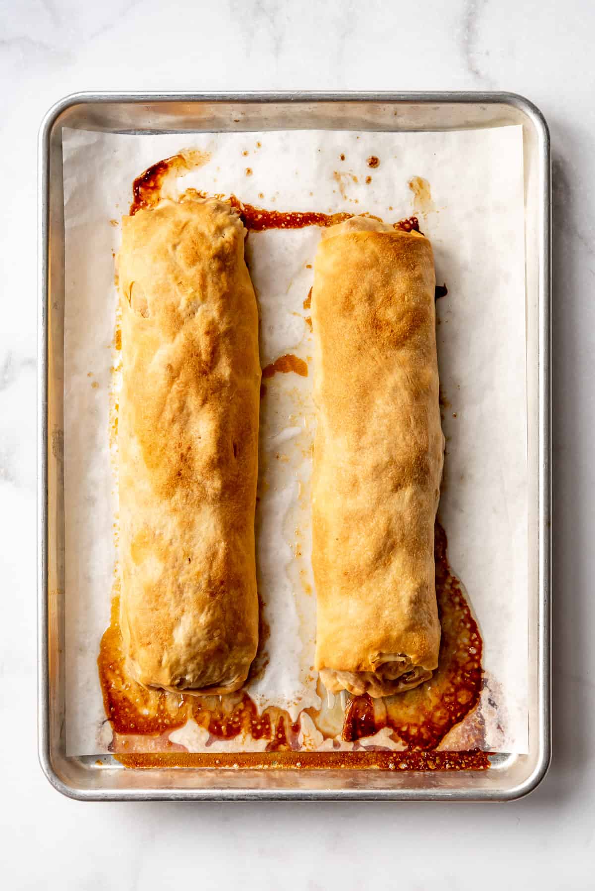 an overhead image of two long rolls of apple strudel before being sliced on a baking sheet lined with parchment paper.