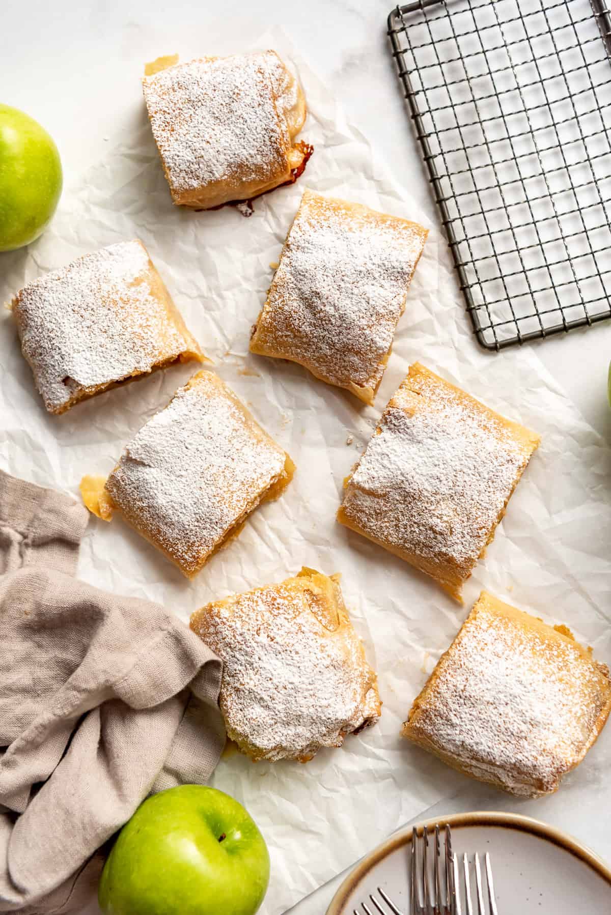 an overhead image of apfelstrudel slices next to a brown linen napkin and green apples.