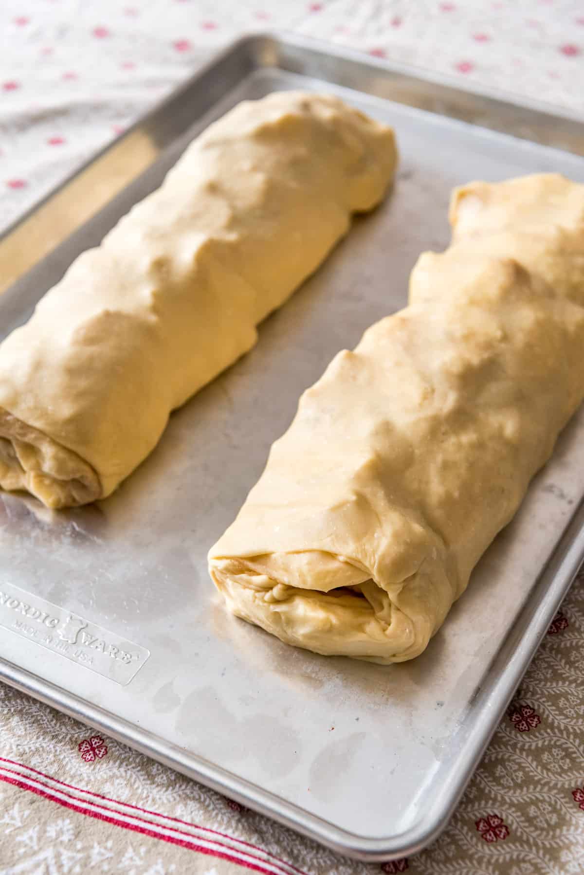 two rolls of apple strudel on a baking sheet before being baked.