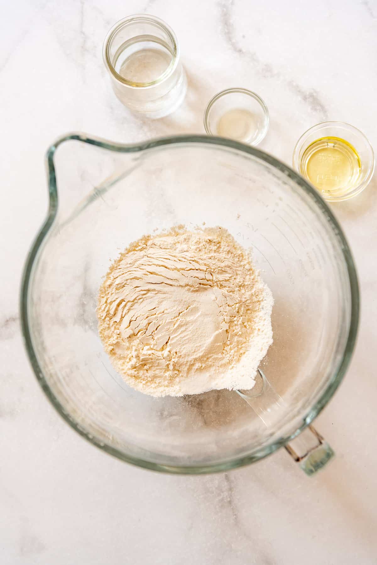 flour and salt in a large glass bowl next to smaller bowls of water, lemon juice, and oil.