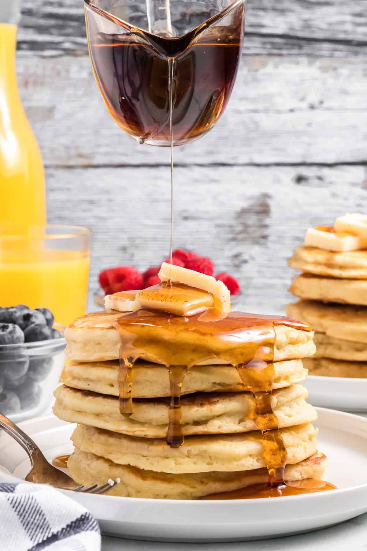 Pouring maple syrup onto a large stack of pancakes.