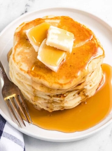 A white plate with a stack of homemade buttermilk pancakes topped with butter and syrup.