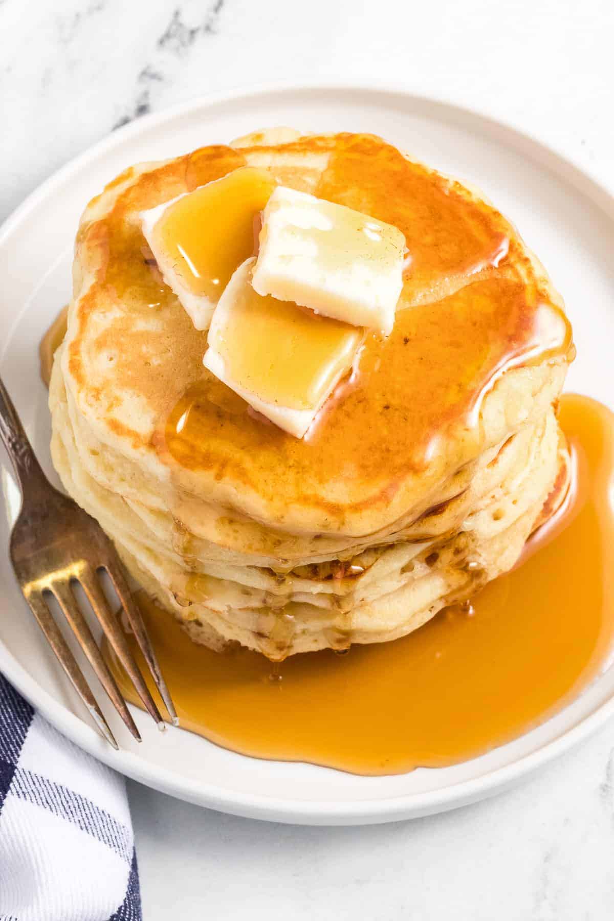 A white plate with a stack of homemade buttermilk pancakes topped with butter and syrup.