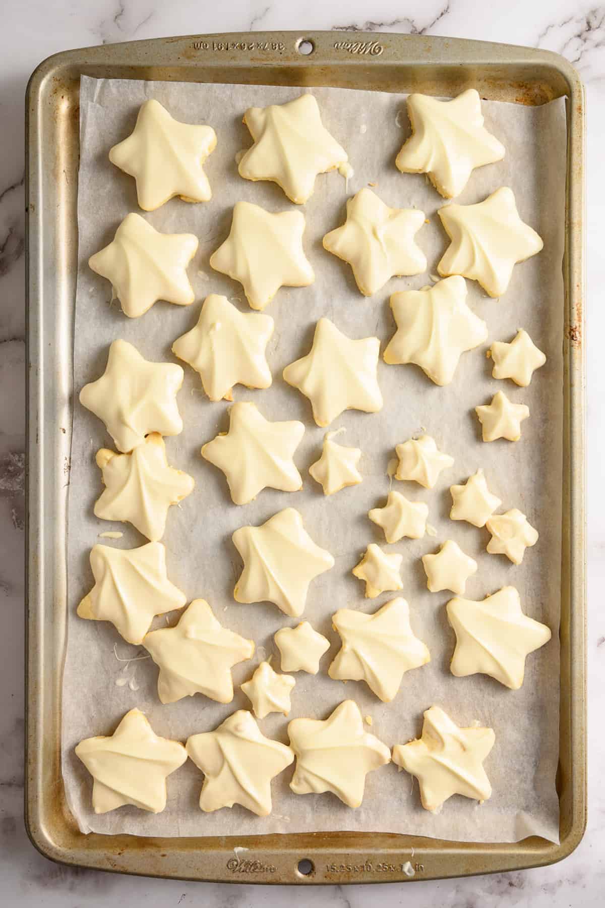 White chocolate covered Christmas star cookies on a baking sheet.