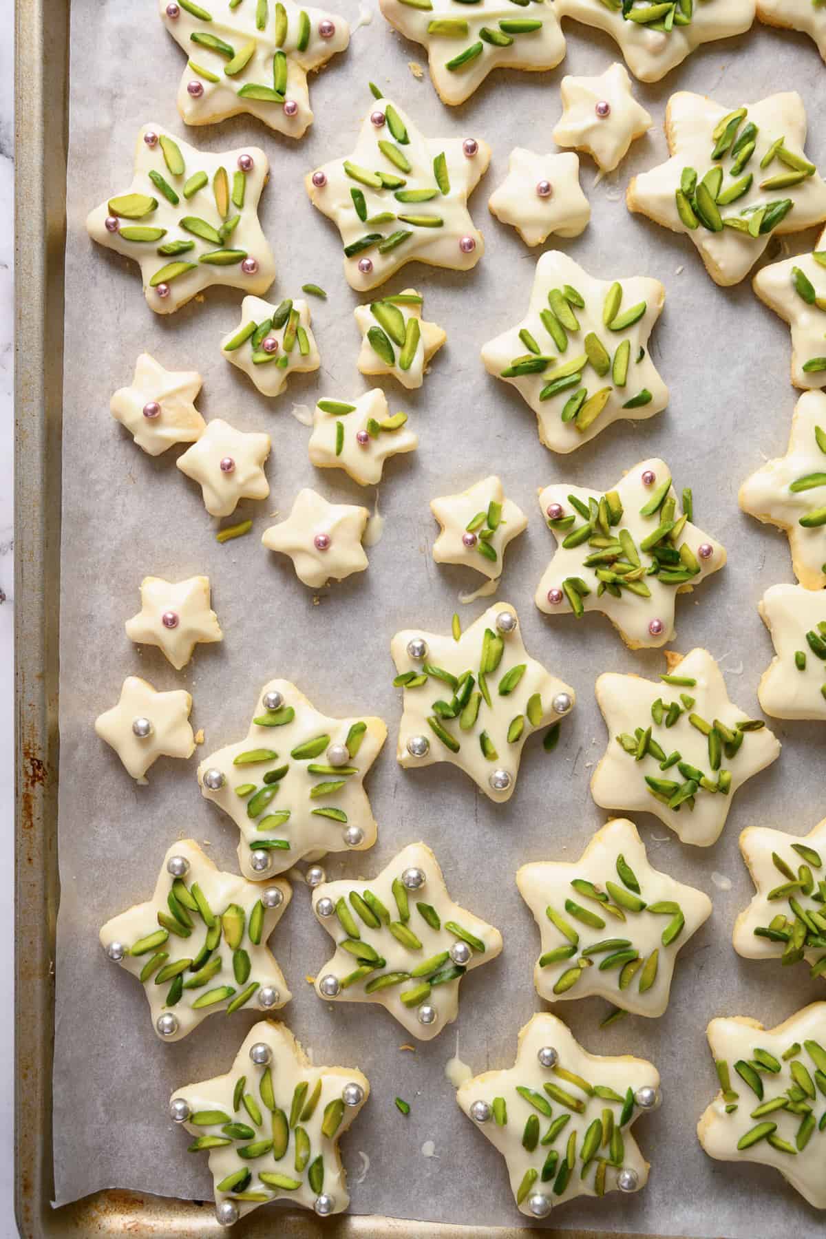 An overhead image of Christmas star cookies decorated with white chocolate and pistachios.