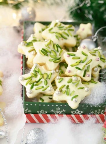 A tin of Christmas star cookies decorated with pistachios.