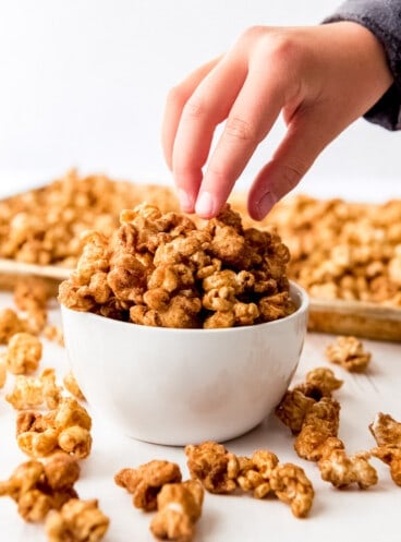 Close up of a white bowl piled high with churro popcorn with a hand reaching in and grabbing some pieces.
