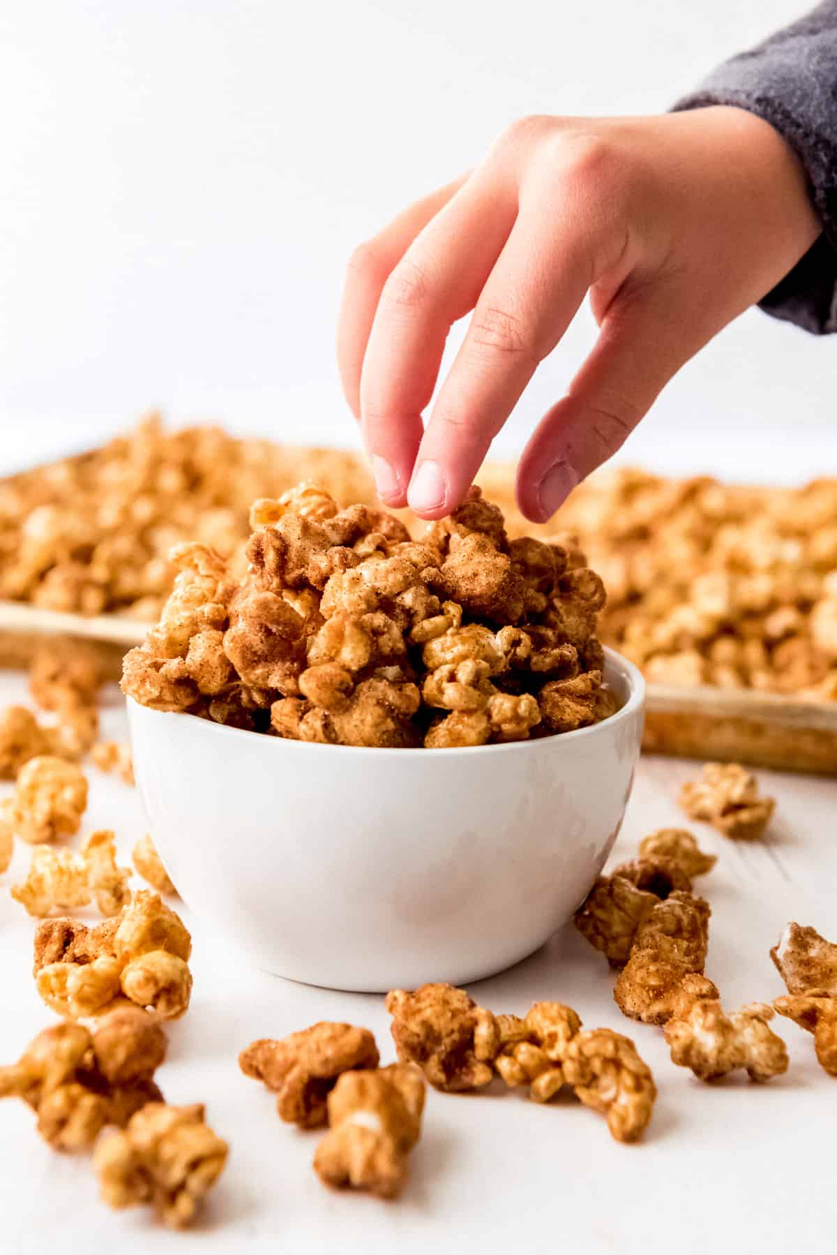 Close up of a white bowl piled high with churro popcorn with a hand reaching in and grabbing some pieces. 