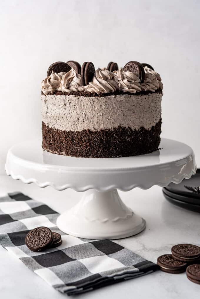 An entire cookies & cream cake decorated with crusted Oreos on a white cake stand.