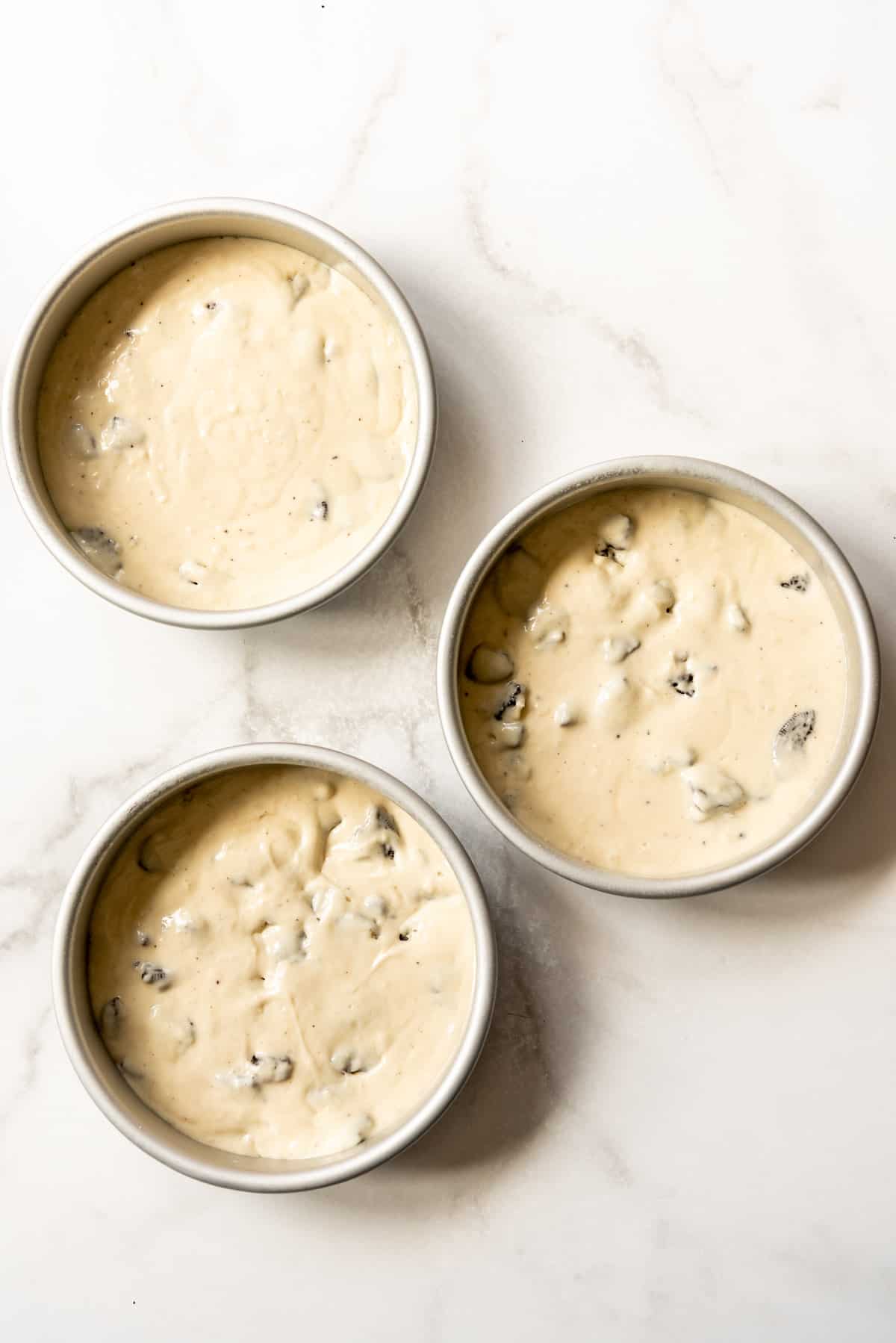 Three 8-inch cake pans filled with cookies & cream cake batter.