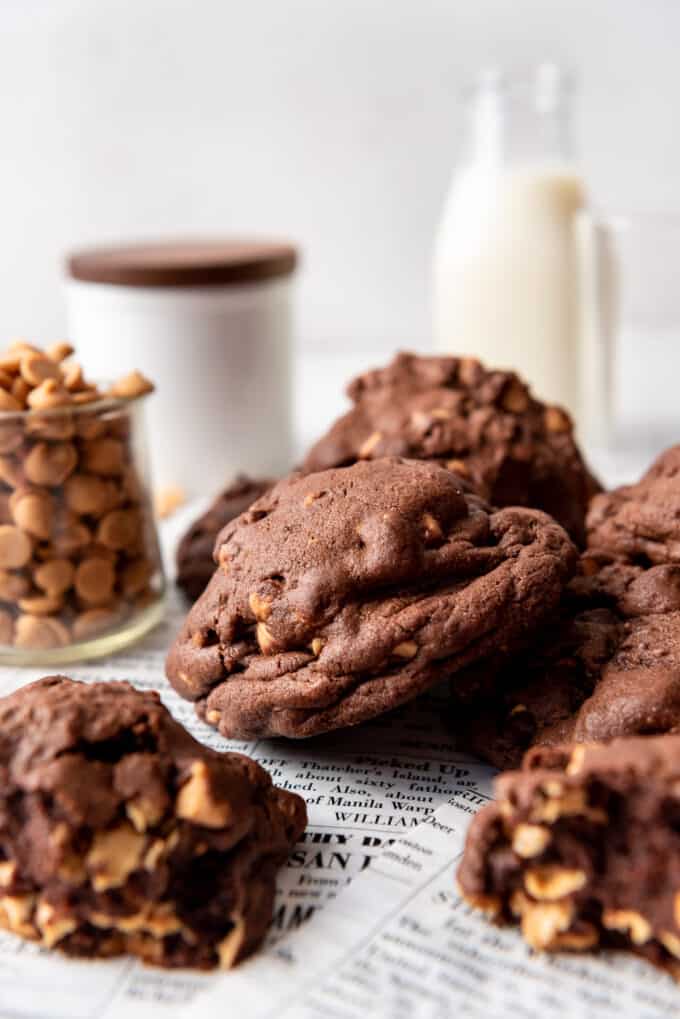 Large dark chocolate cookies with peanut butter chips next to a jar of peanut butter chips.