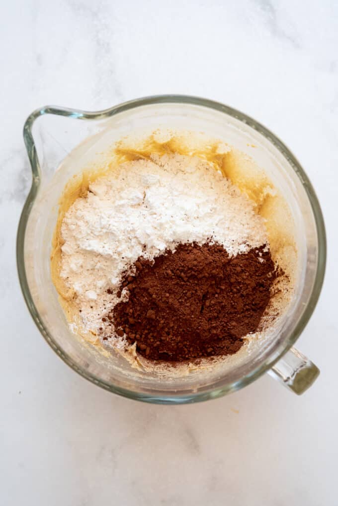 Adding cocoa powder and flour to a bowl to make cookie dough.