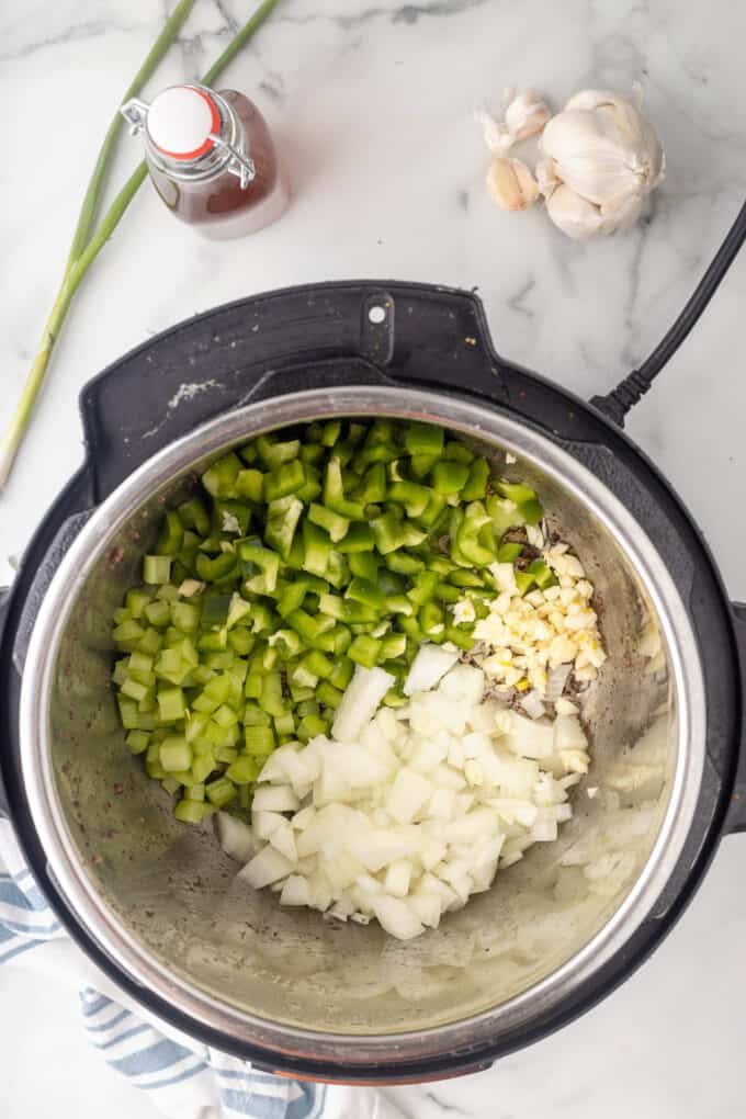 Adding chopped onions, celery, green bell pepper, and garlic to an instant pot.