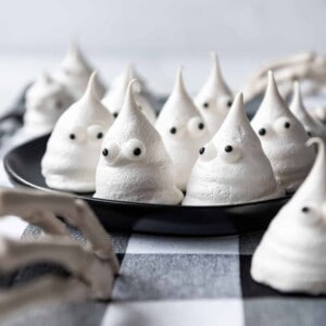Ghost meringue cookies with candy eyes on a black plate.