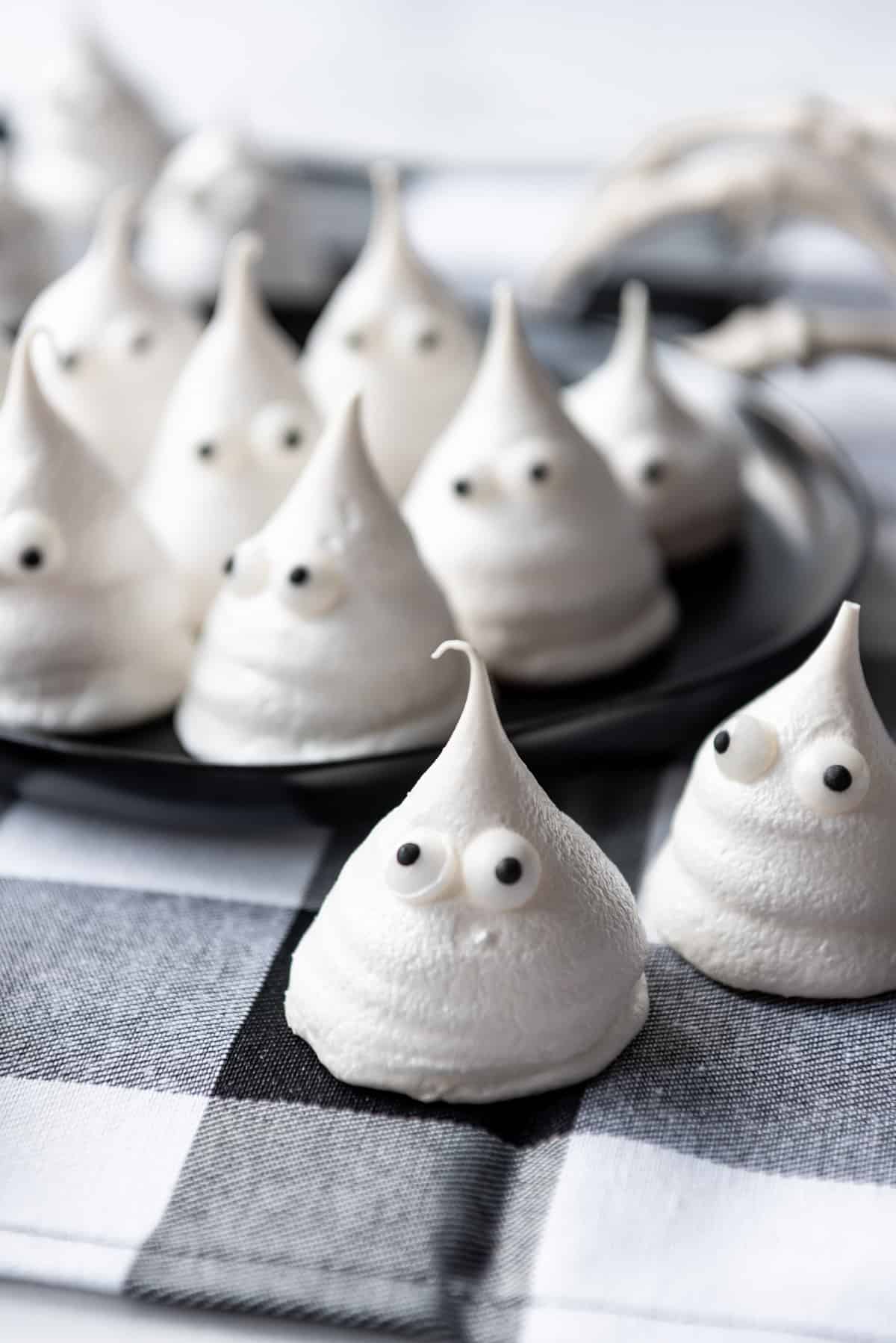 Ghost meringue cookies on a black checkered linen napkin and black plate.