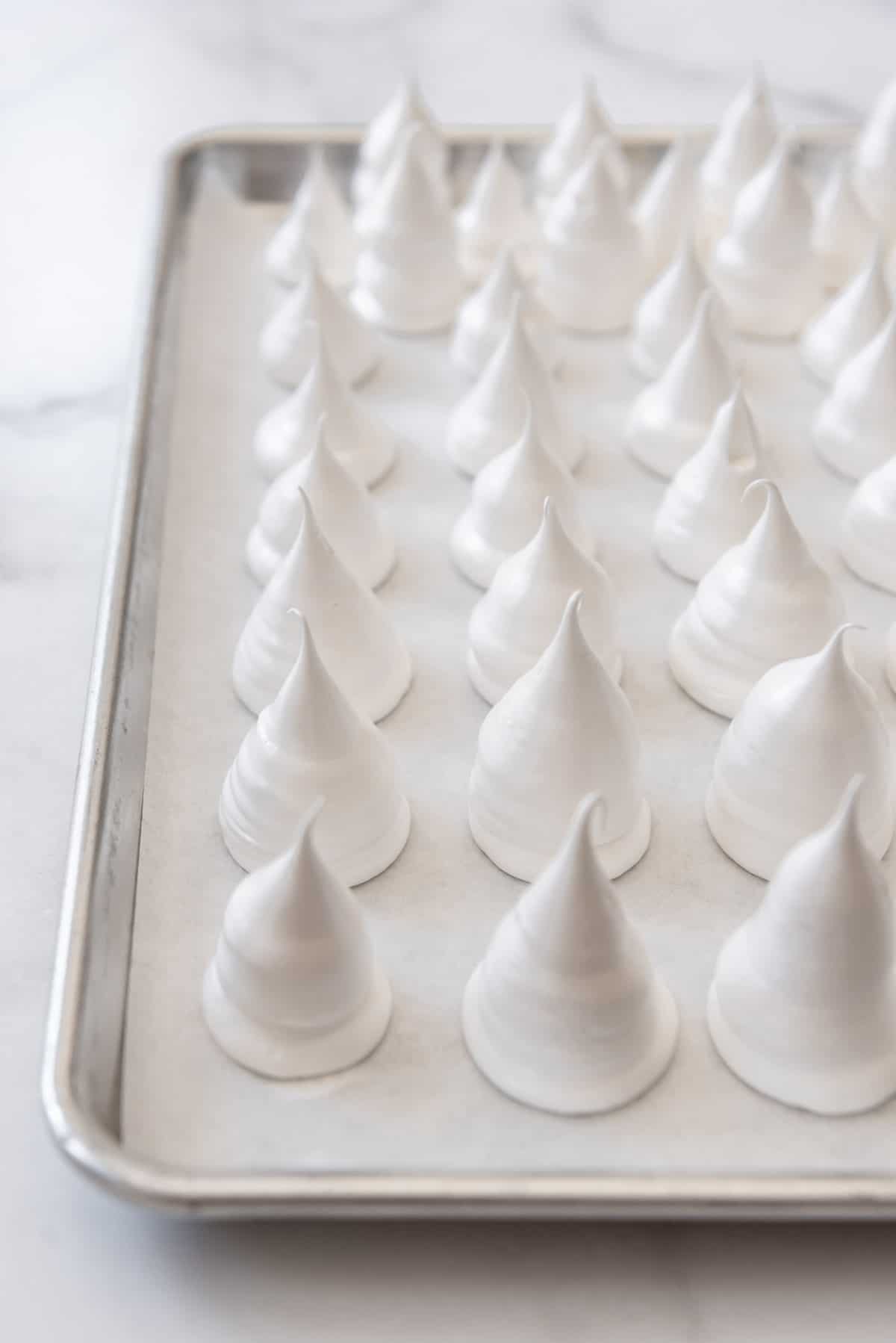 Mounds of piped meringue on a baking sheet.