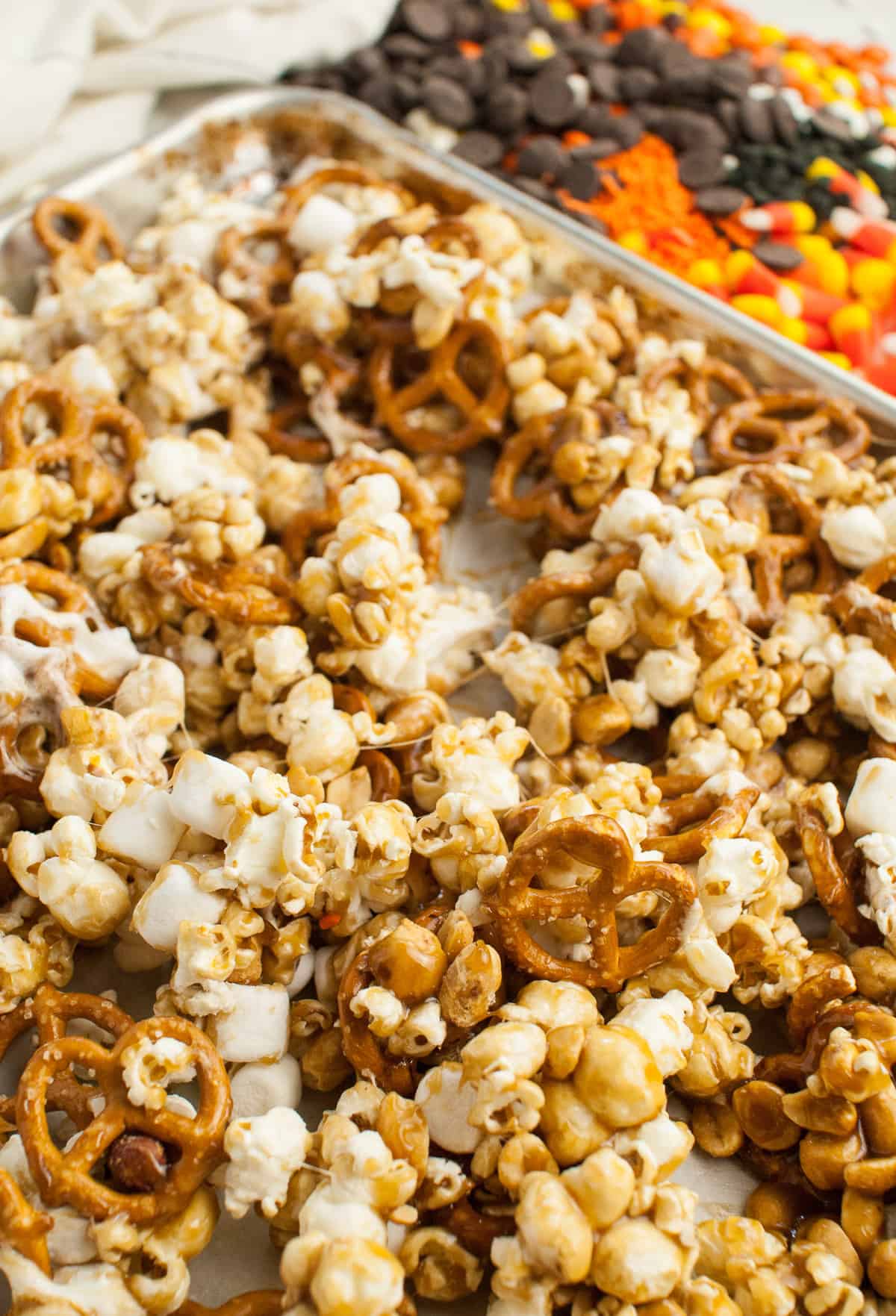 Gooey marshmallows, pretzels, popcorn, and peanuts in a caramel sauce on a baking sheet.