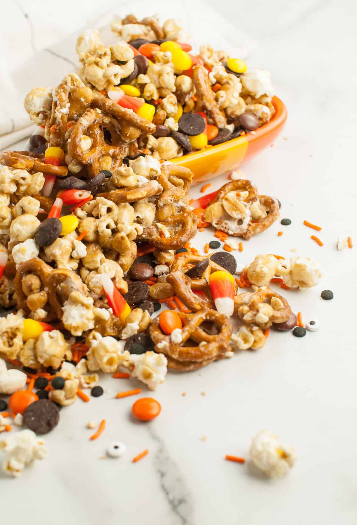 Halloween caramel corn snack mix with peanut, pretzels, and M&Ms spilling out of a bowl.