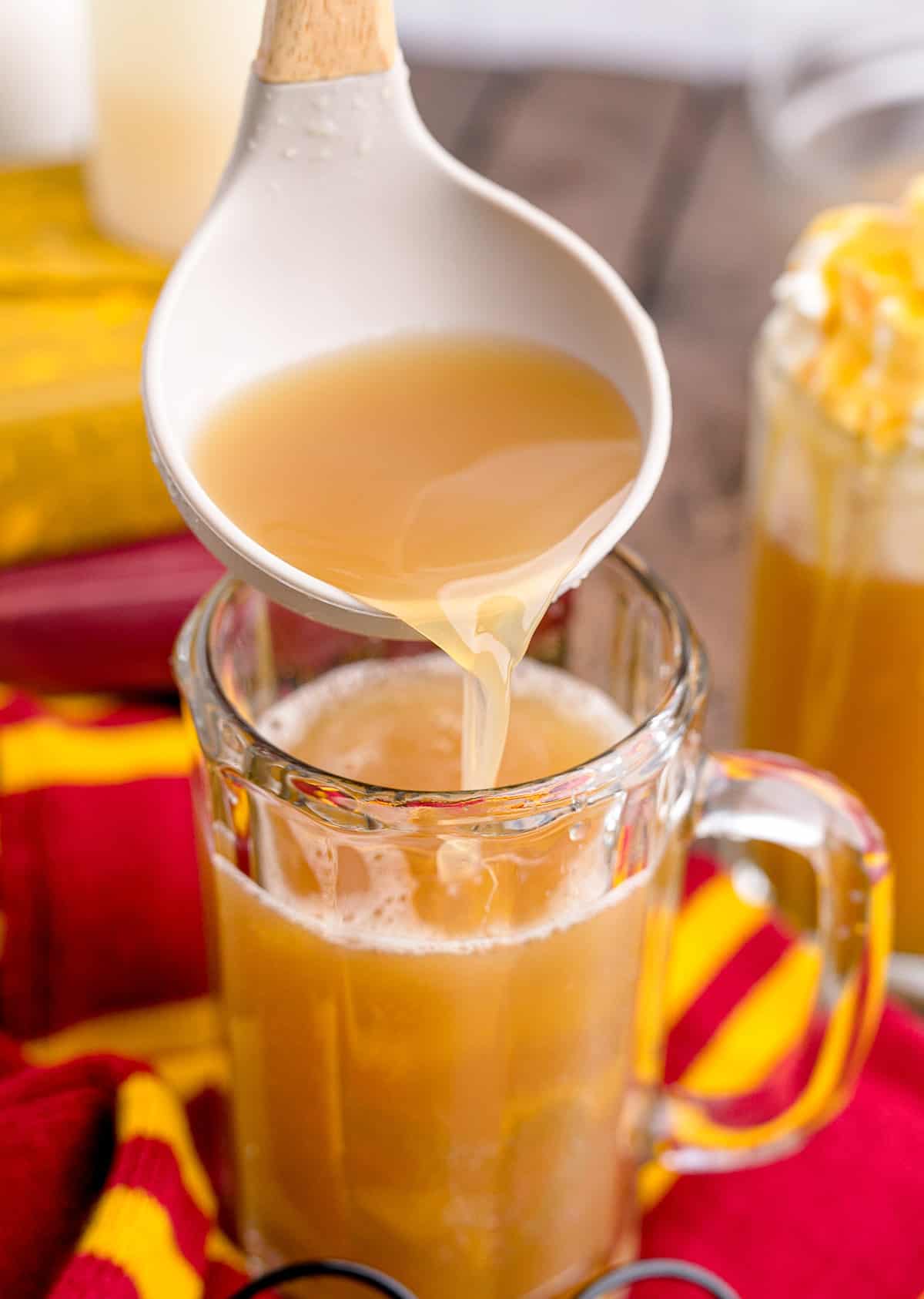 Ladling homemade butterbeer into a large glass mug.