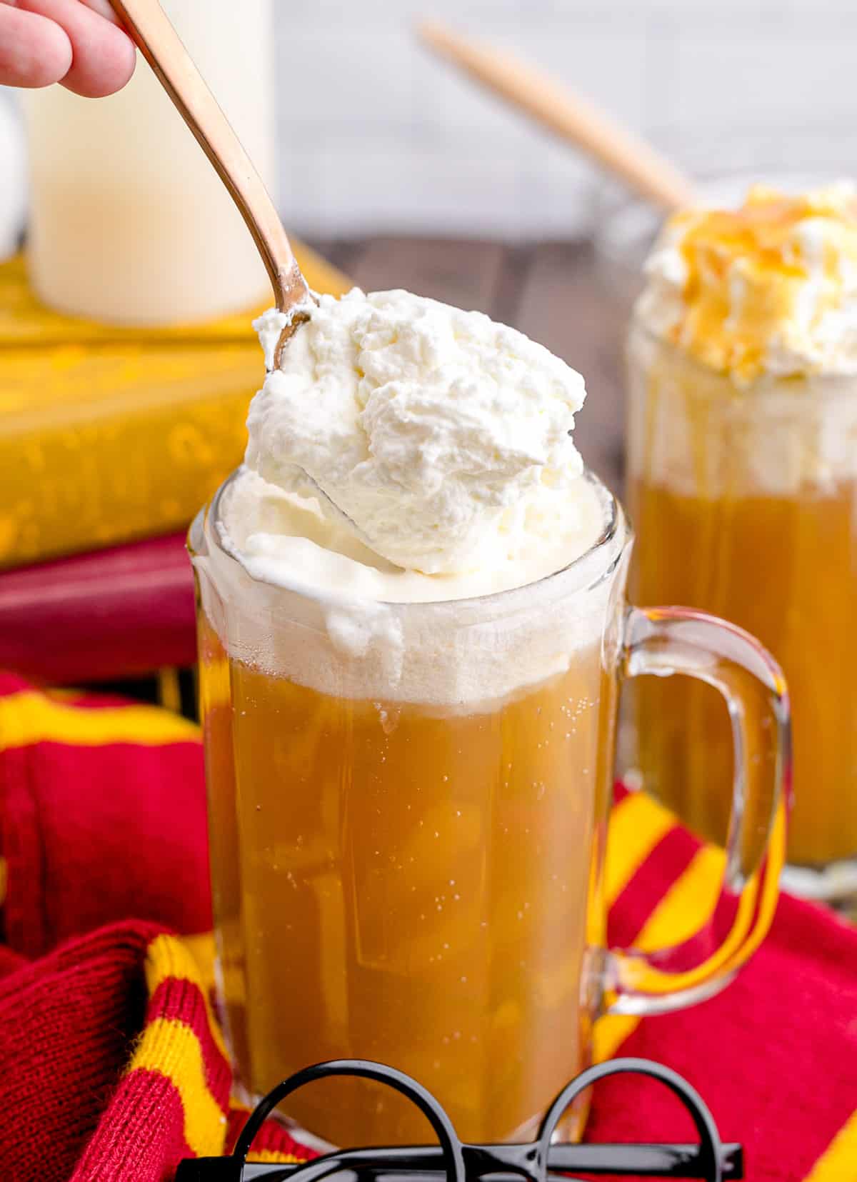 Spooning homemade whipped cream onto a mug full of Harry Potter copycat butterbeer.