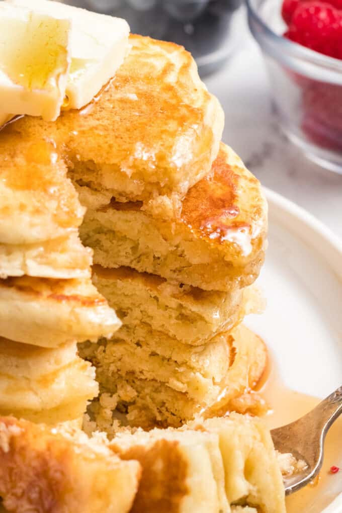 A tall stack of pancakes with a bite taken out of them.
