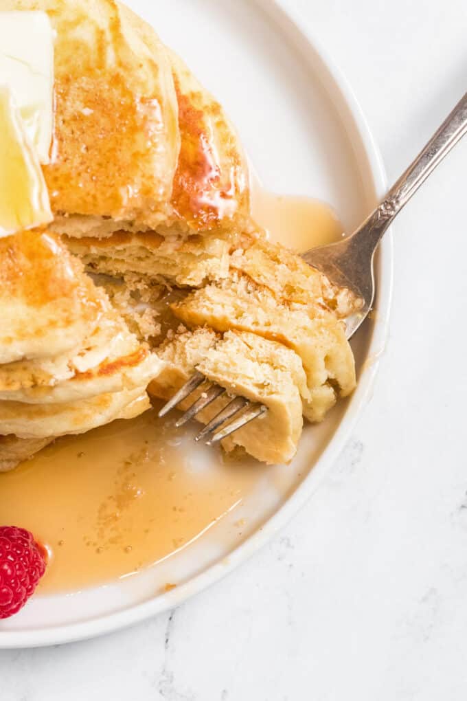 A fork with bites of fluffy homemade pancake on it in a pool of maple syrup.
