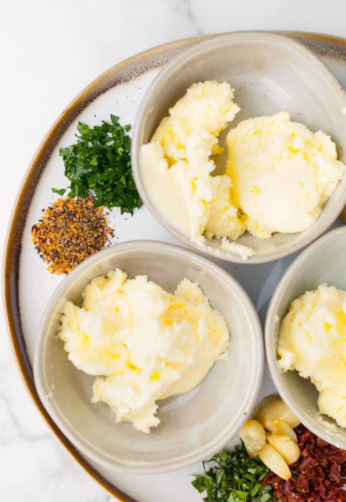 Bowls of homemade butter with herbs, spices, and garlic next to them.