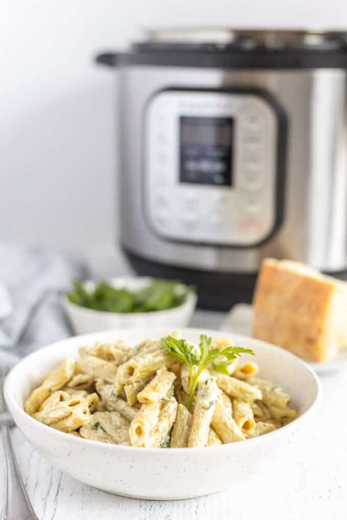 A bowl of creamy penne alfredo pasta in front of an Instant Pot pressure cooker.