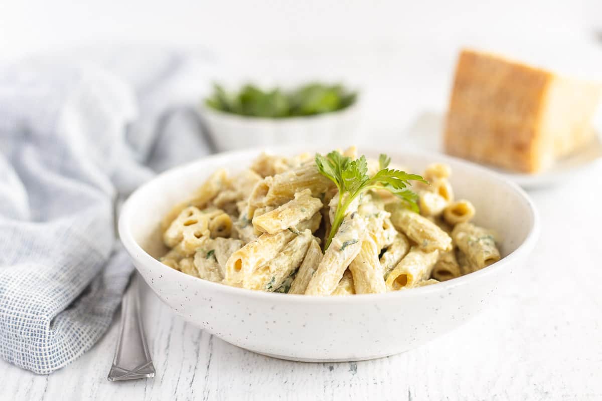 Instant Pot Creamy Penne Alfredo in a white bowl topped with fresh parsley on a white table. 