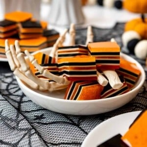 Black, orange, and white striped layered Halloween Jello squares in a bowl with plastic skeleton hands.