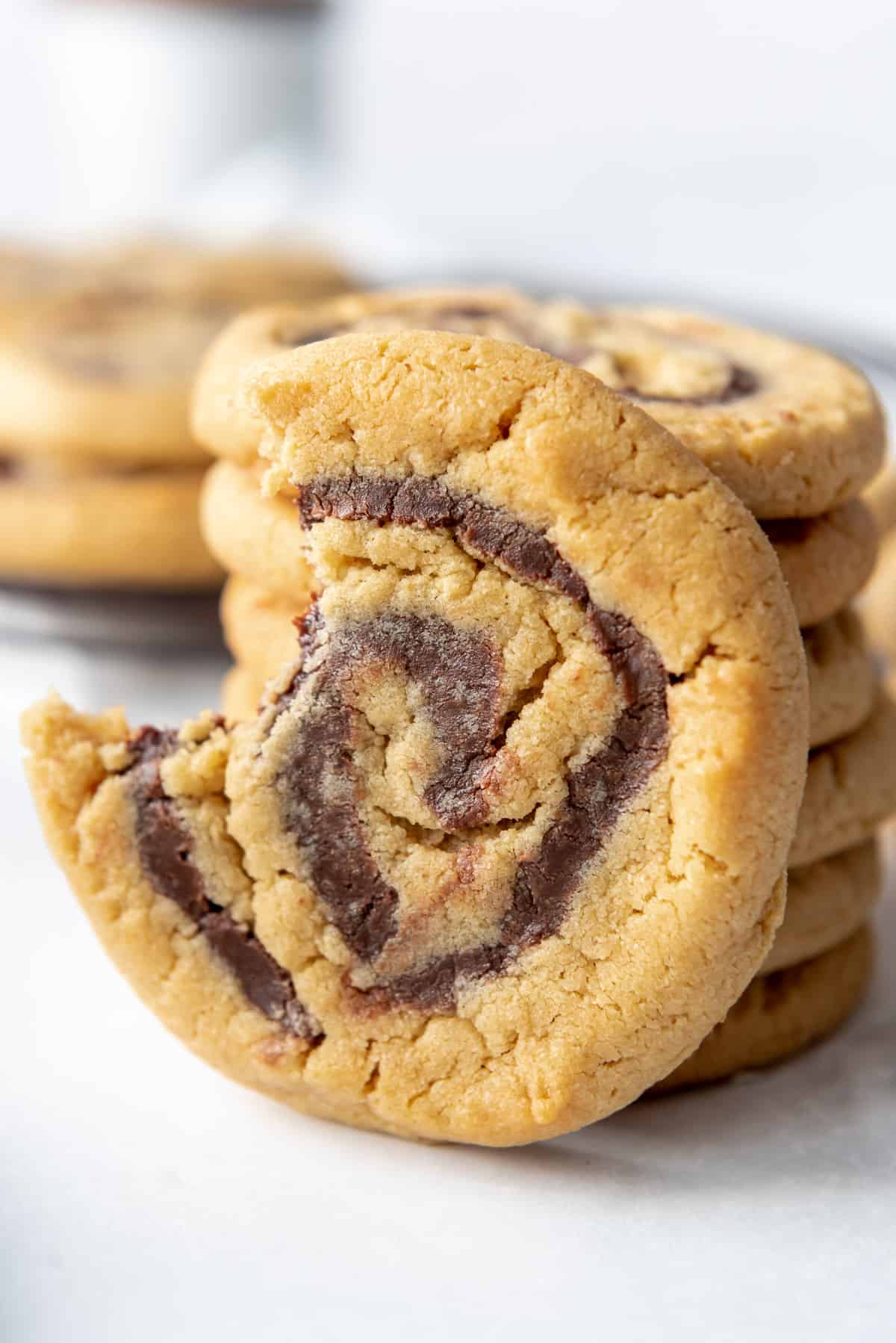 A peanut butter chocolate whirligig pinwheel cookie with a bite taken out of it leaning against a stack of cookies.