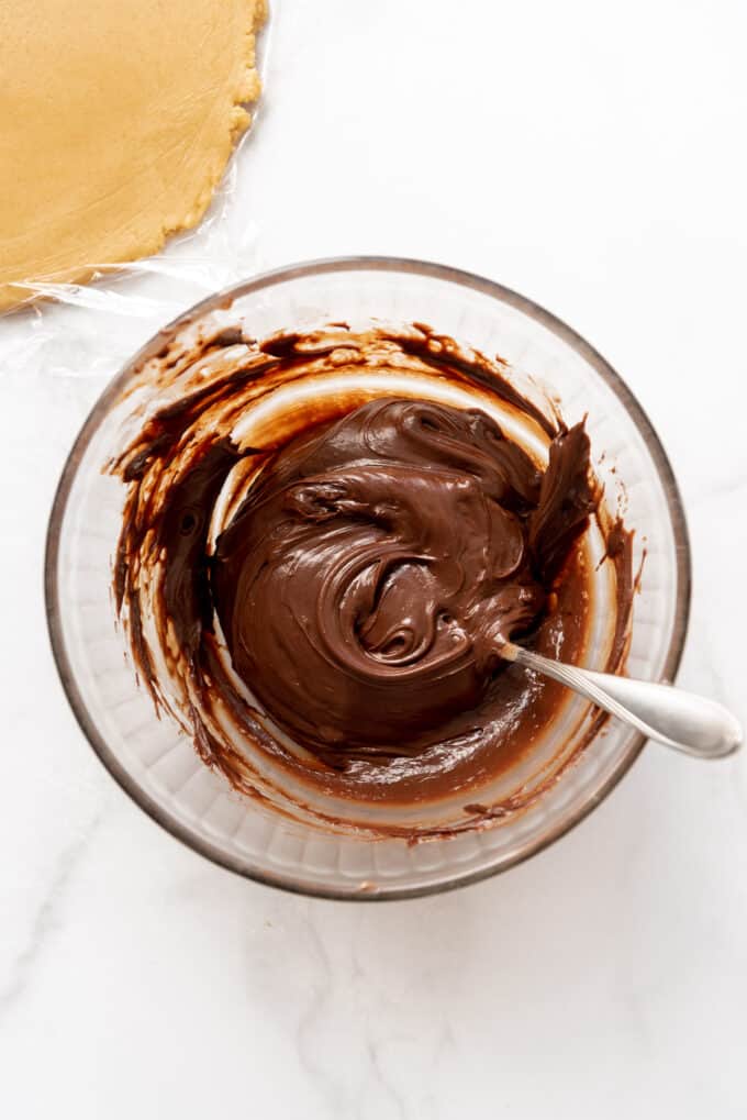 Stirring chocolate, butter, and sweetened condensed milk in a bowl until melted.
