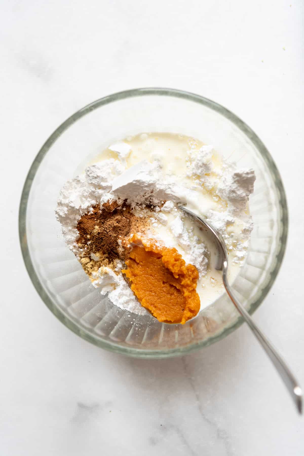 Pumpkin, powdered sugar, cinnamon, and heavy cream in a bowl with a spoon.