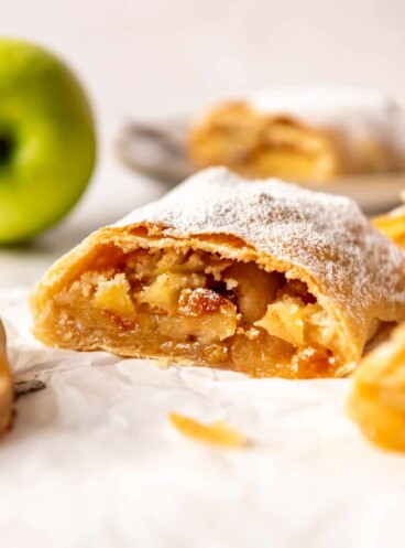 a slice of German apple strudel with raisins in front of a Granny Smith apple.