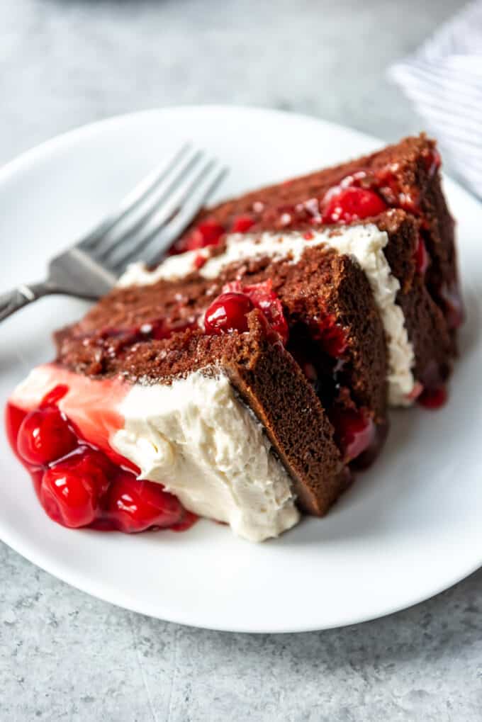 A slice of chocolate black forest cake with ermine frosting and cherries.
