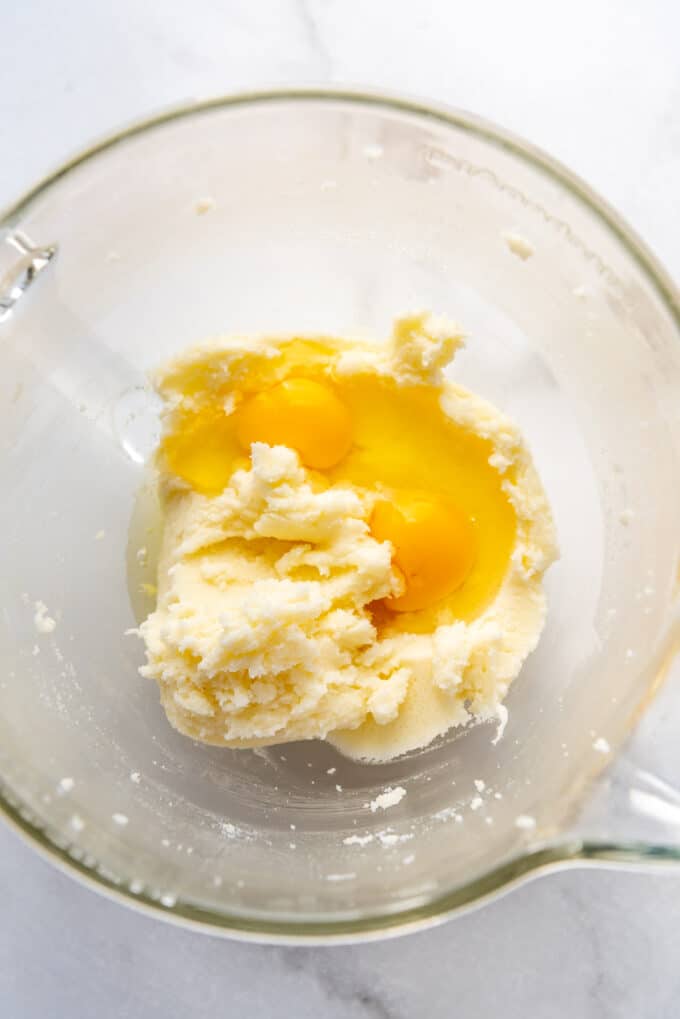 Adding eggs to creamed butter and sugar in a mixing bowl.