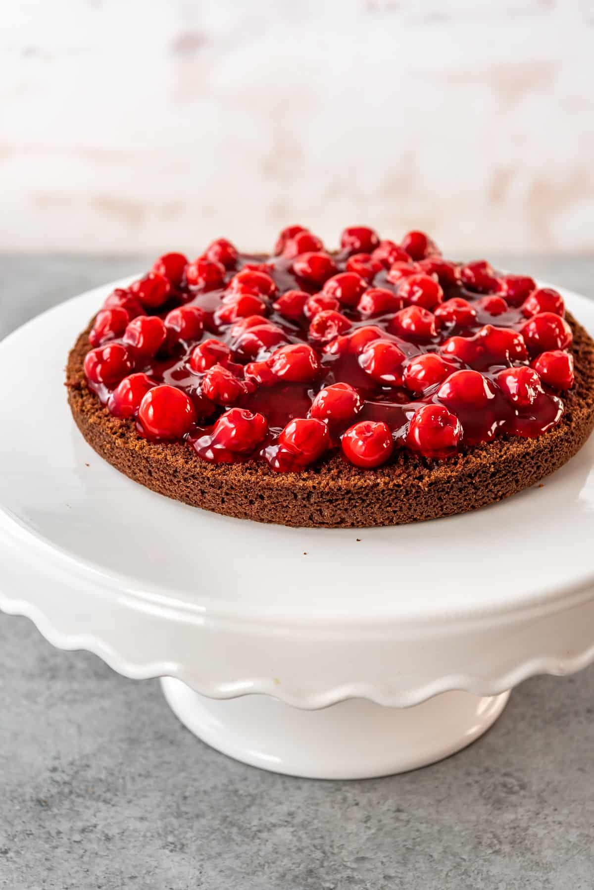 Assembling a black forest cake by adding a layer of cherries onto the chocolate cake layer.