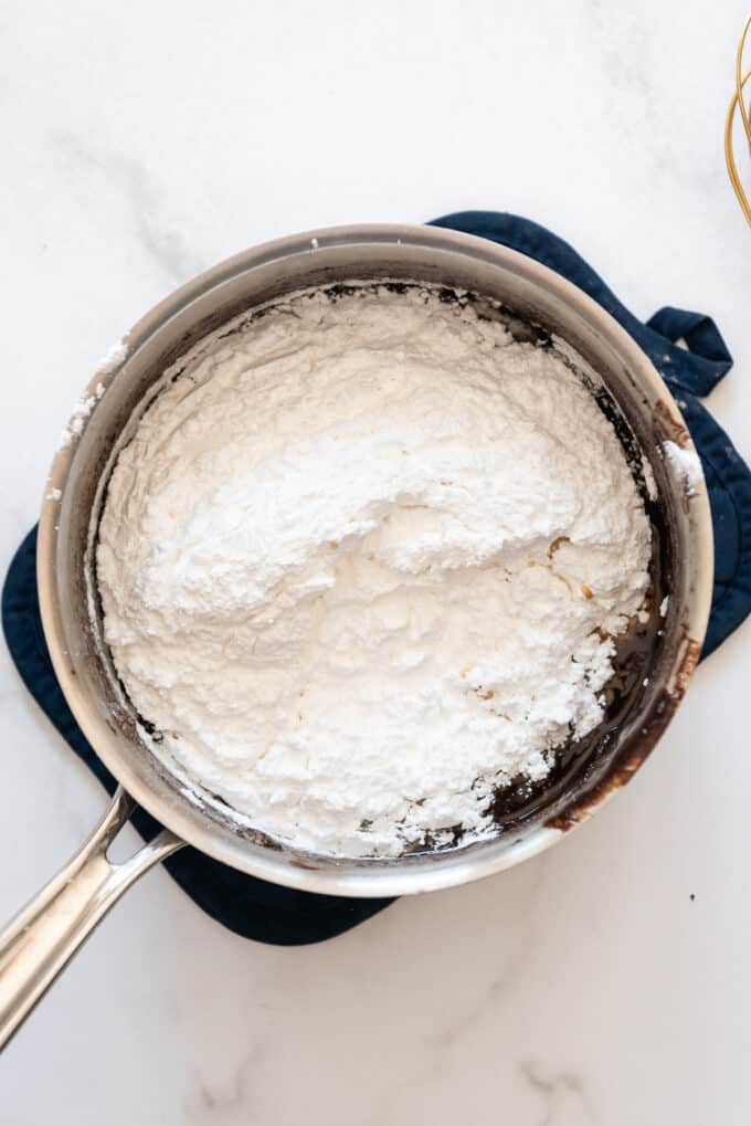 Adding powdered sugar to a cooked fudge frosting in a saucepan.