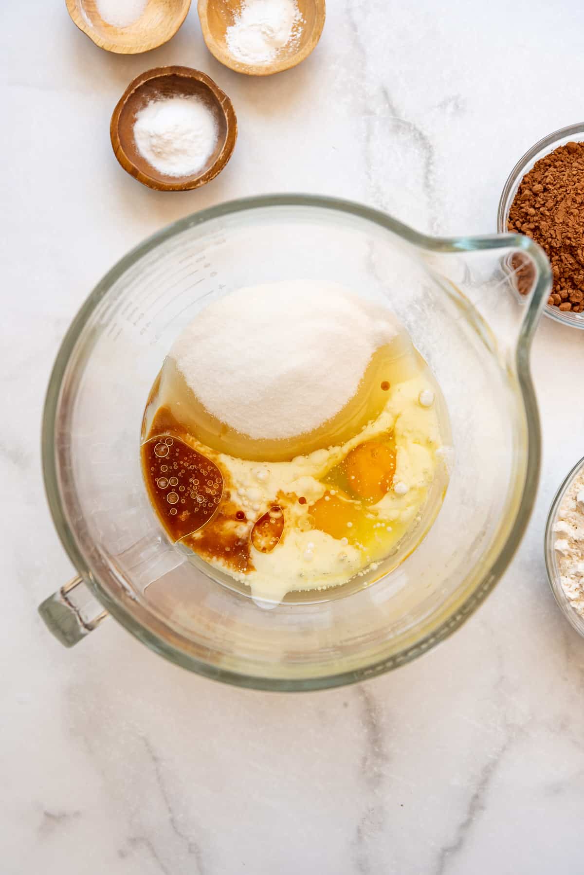 Combining granulated sugar, eggs, milk, and vanilla extract in a glass mixing bowl.