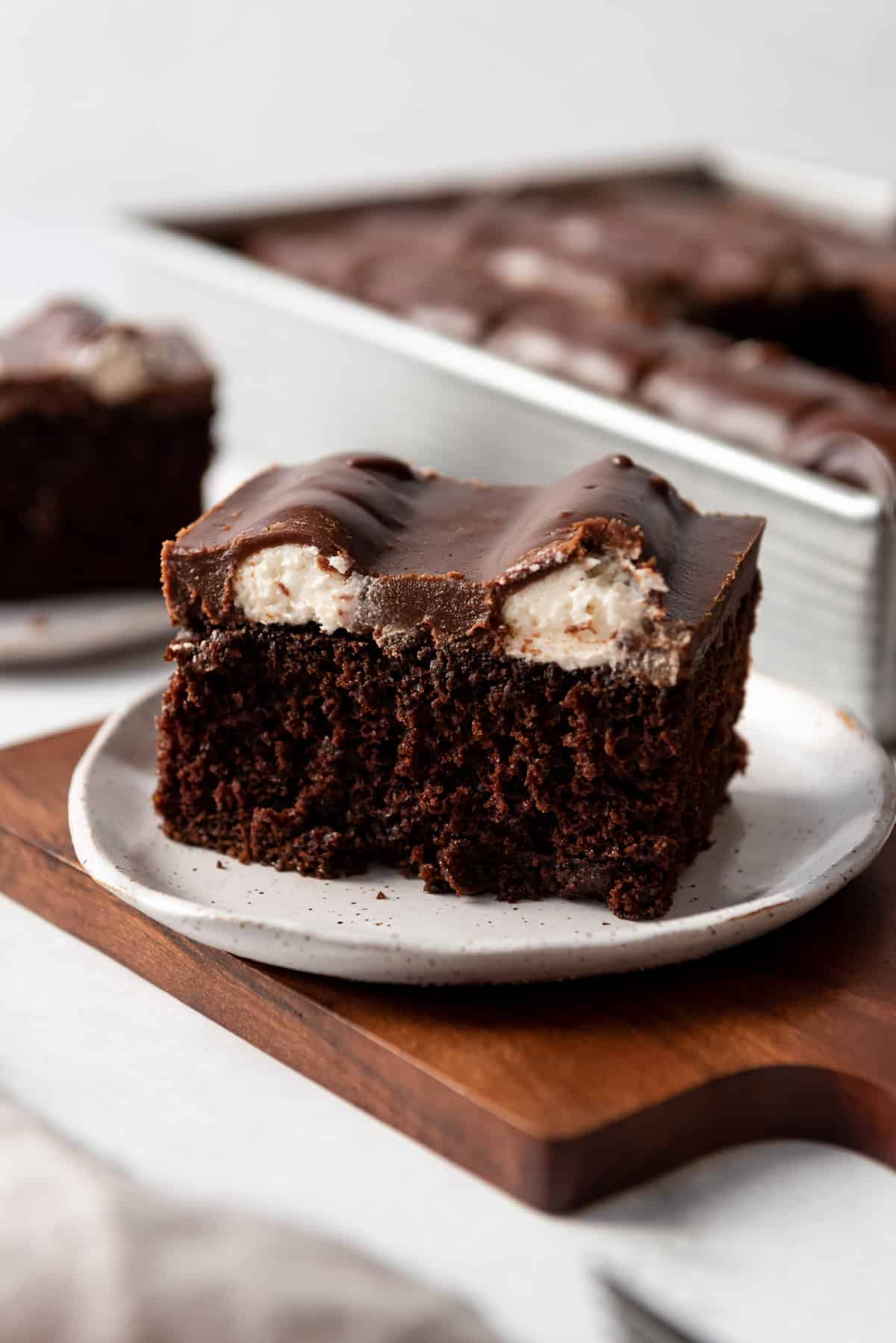 A slice of moist chocolate cake with white buttercream lines and chocolate fudge frosting on top.