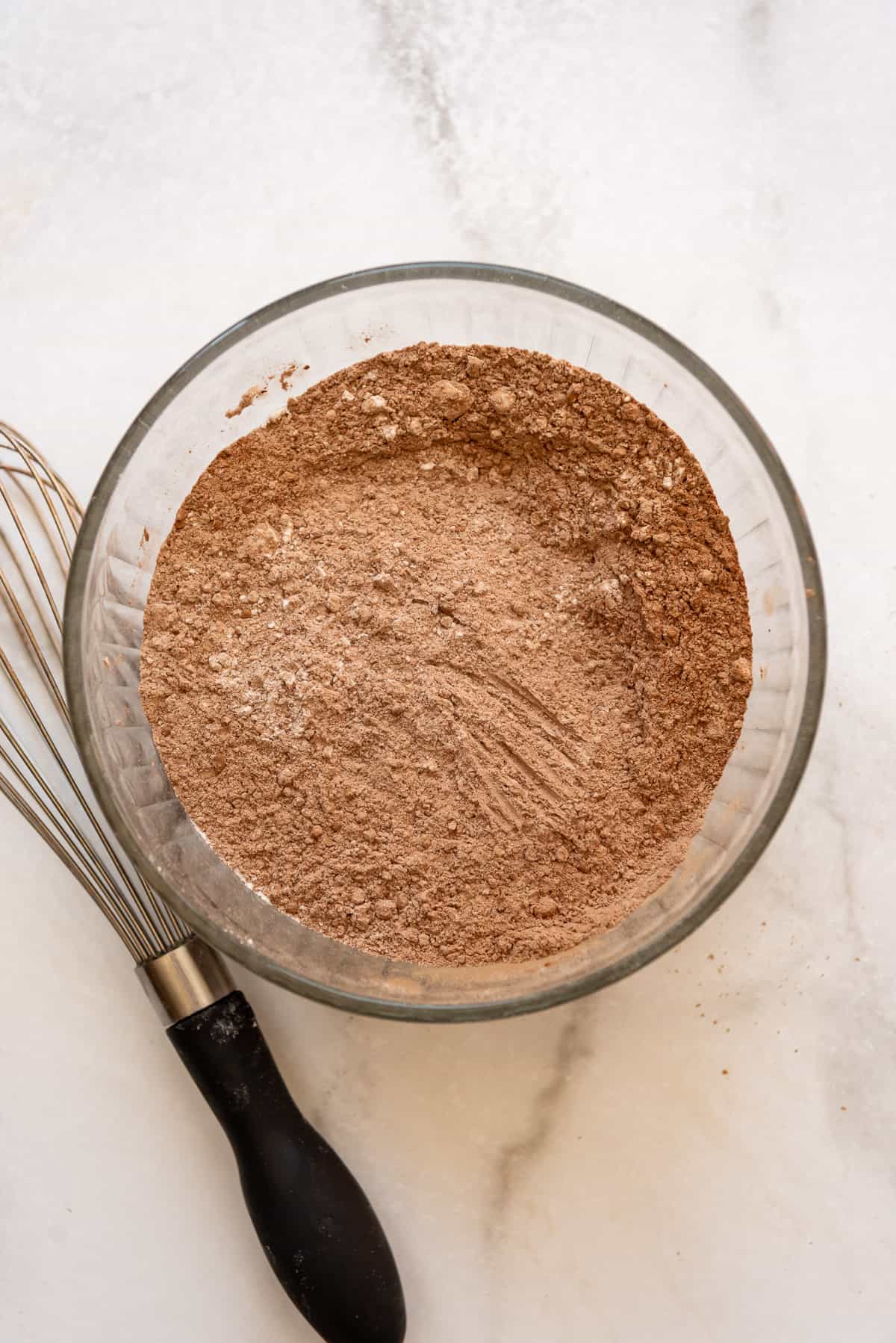 Whisked dry ingredients in a bowl next to a whisk.