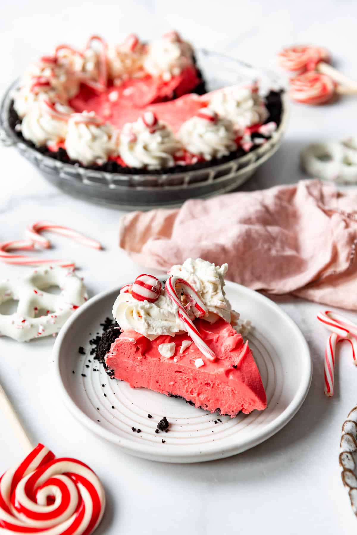 A slice of peppermint pie on a white plate in front of the whole pie.