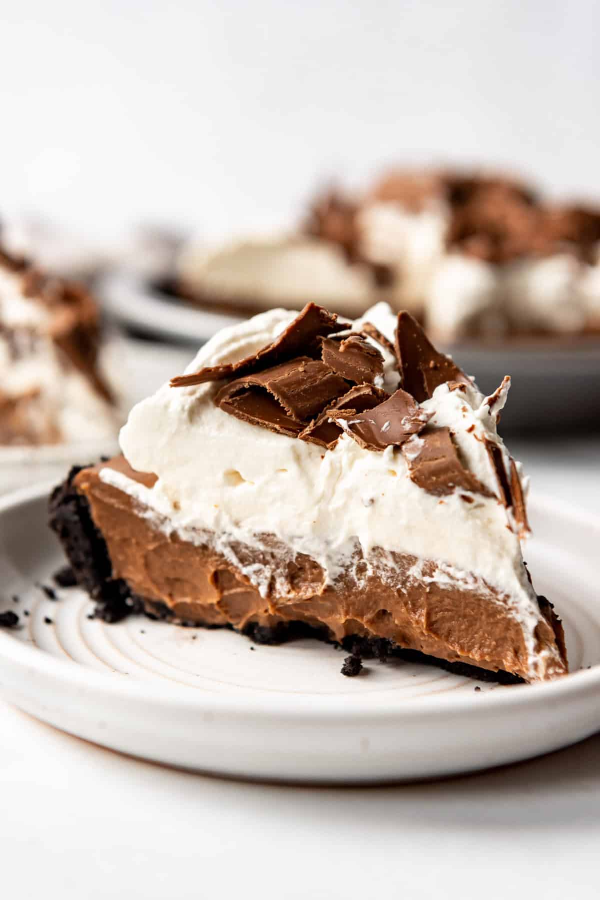 A slice of chocolate cream pie topped with whipped cream and chocolate curls on a white plate.