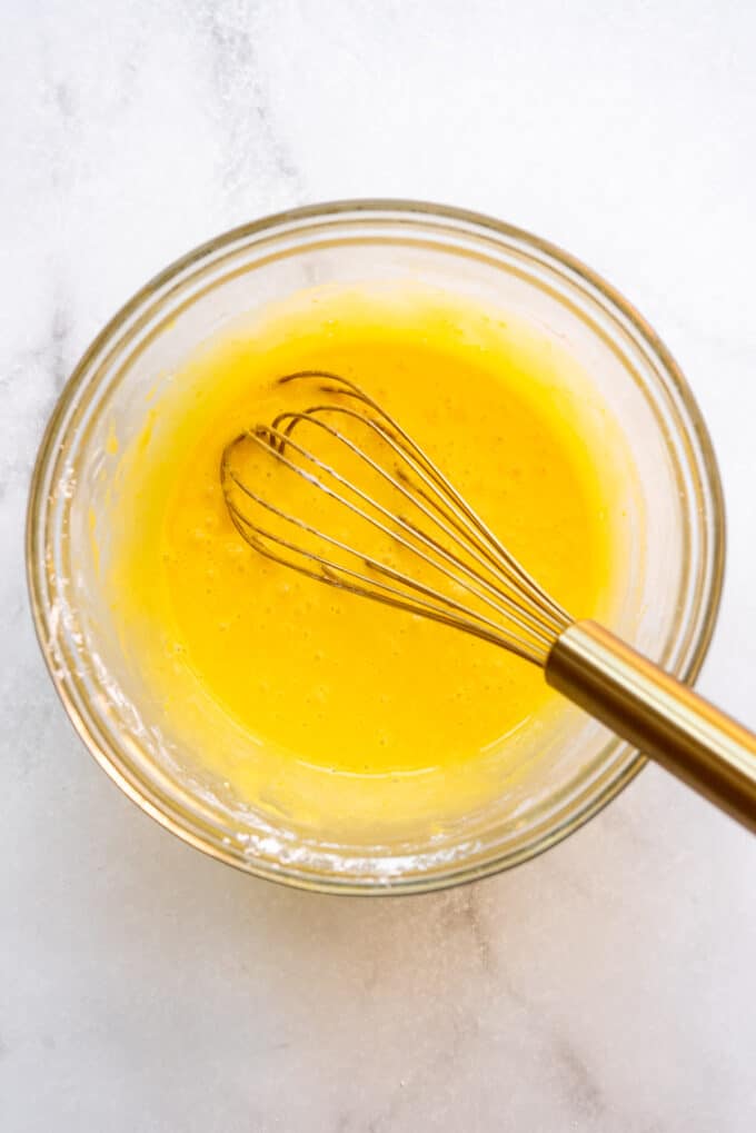An image of sugar, cornstarch, and egg yolks in a bowl with a whisk to be made into a cream pie filling.