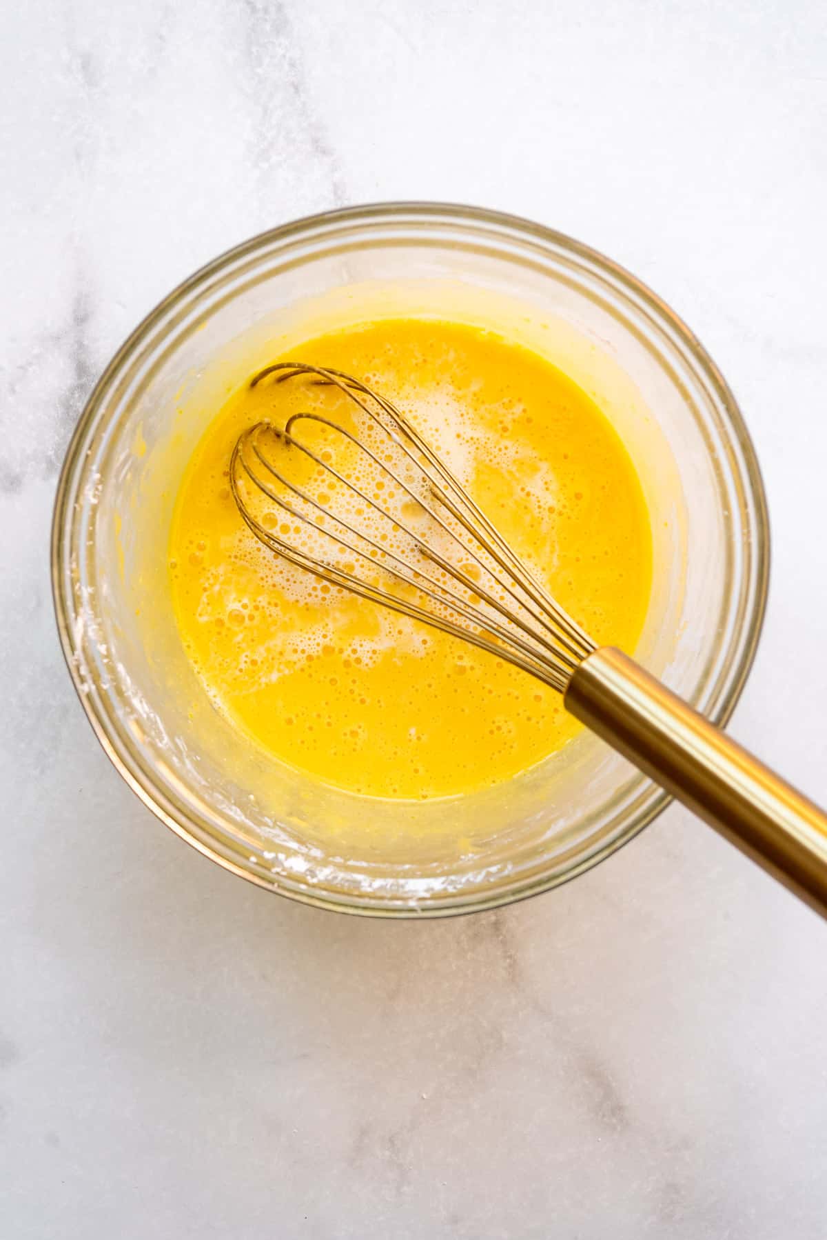 Adding heated milk and cream to an egg yolk and sugar mixture in a glass bowl.