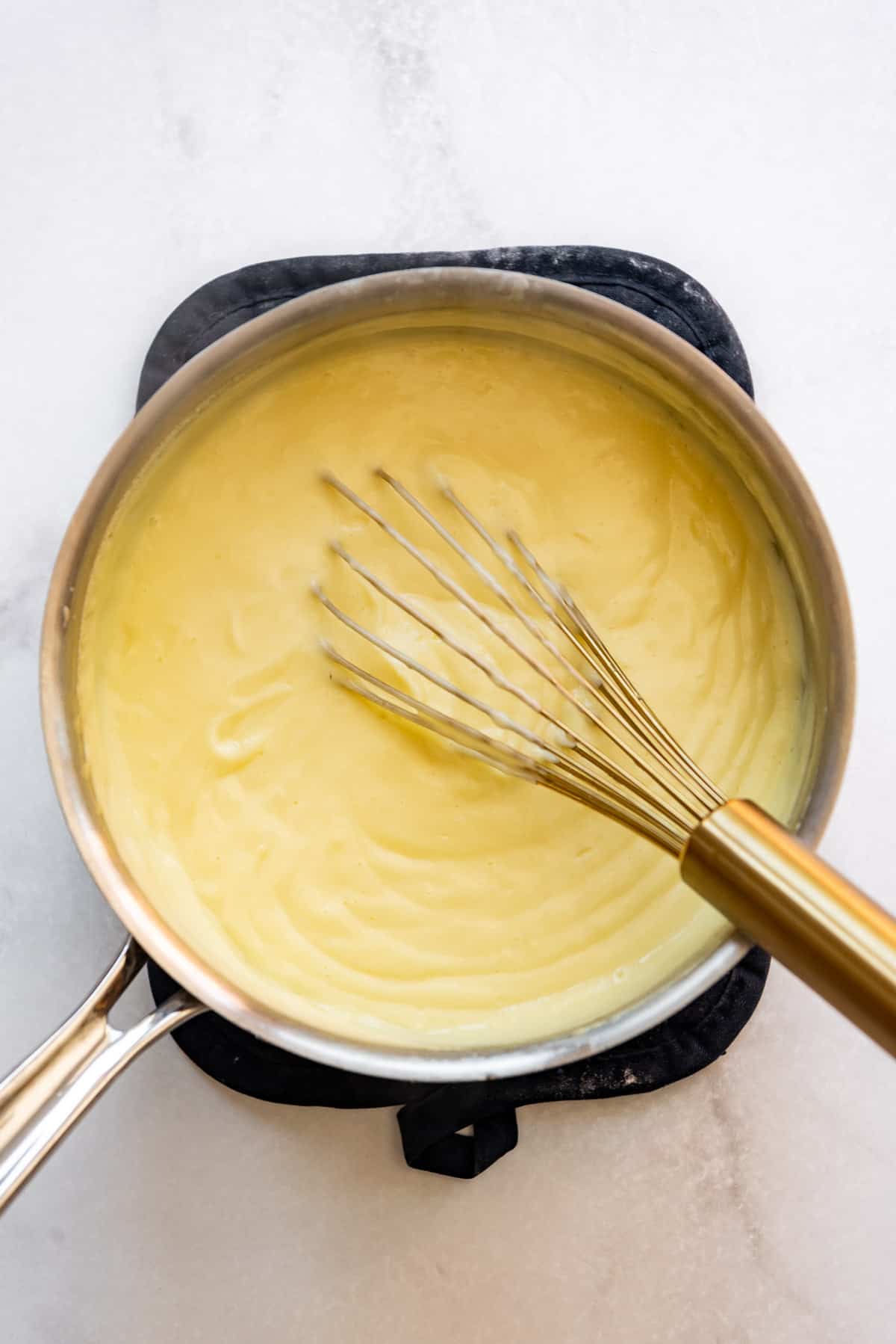 Heating tempered egg yolks and cornstarch in a milk and cream mixture in a saucepan until thick.