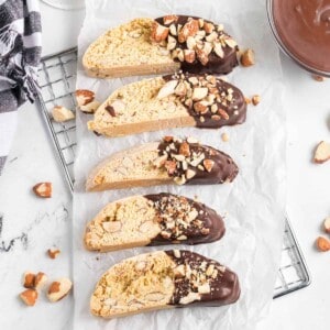 Five pieces of almond biscotti decorated with semisweet chocolate and toasted nuts.