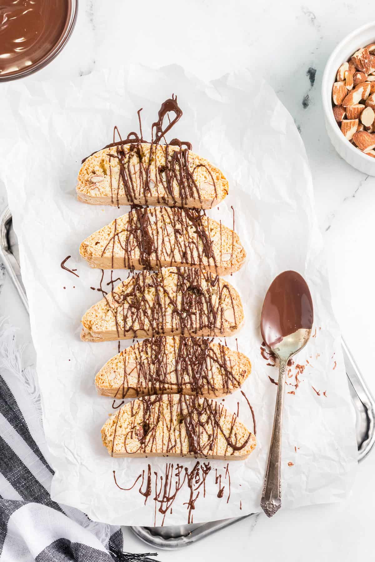 Using a spoon to drizzle melted dark chocolate on almond biscotti.